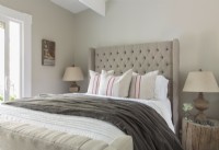 The apartmentâ€™s tall ceilings can accommodate the tufted shelter bed with footboard. The neutral palette of linens is kept lively with the variety of textures. 