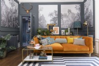 Orange velvet sofa in a grey living room with panels infilled with monochrome tropical tree patterned wallpaper