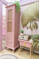 Tall pink upcycled cabinet and reclaimed pink painted vintage sewing table in a pink conservatory with gold tropical fern table lamp