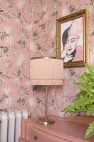 Fringed art deco style table lamp on a reclaimed chest of drawers in front of palm leaf patterned wallpaper

