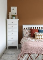Tall white chest of drawers against brown painted wall in bedroom