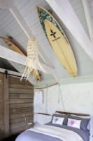 Sally and John Biddle's house in Cornwall, converted barn bedroom. Wooden beams and rustic decoration, surfboards attached to the ceiling