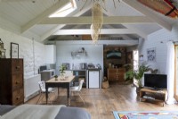 Converted barn, open plan living area with simple kitchen and farmhouse table. Wooden beams and rustic decoration.