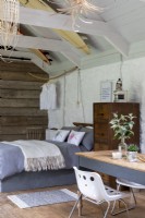 Converted barn, with bed, furniture, and desk. Wooden beams and rustic decoration, surfboards decorating the wooden roof and a simple wooden table