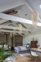 Converted barn, with bed, furniture, and desk. Wooden beams and rustic decoration, surfboards decorating the wooden roof