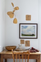 Framed landscape painting and wooden mobile above wooden desk