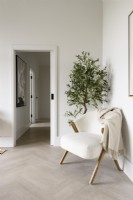 White chair with throw in the corner of a living area in a living room with view along a corridor behind