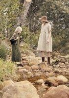 Two women in vintage clothing walking on rocks in stream