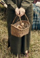 Woman in vintage linen dress holding basket of foraged items