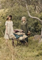 Two women with antique wheelbarrow in woodland