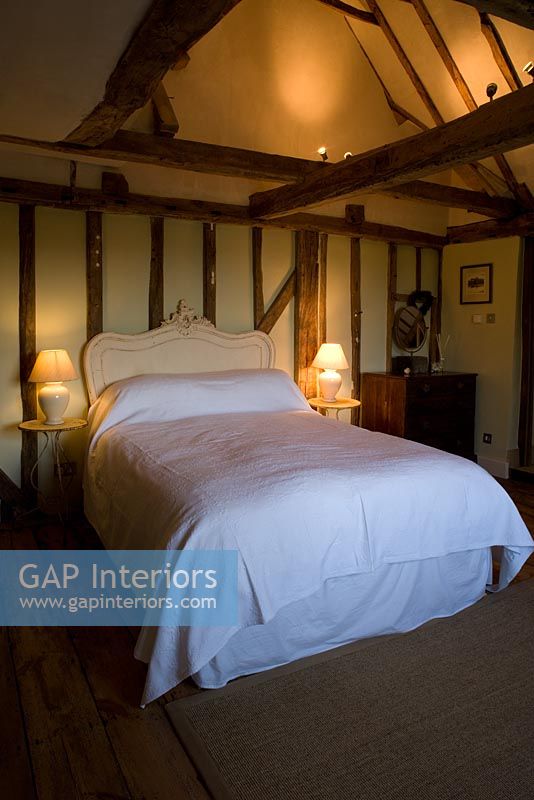 Boonshill Farm, East Sussex. Interior of bedroom exposed beams, french bedhead and old metal side tables. 