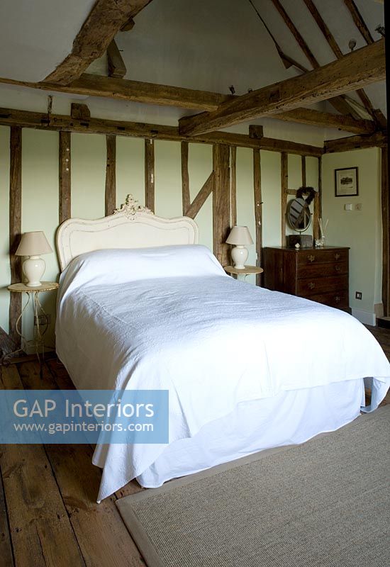 Boonshill Farm, East Sussex. Interior of bedroom with wooden floorboards, exposed beams, french bedhead and old metal side tables. 