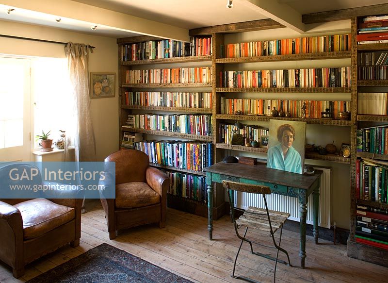 Boonshill Farm, East Sussex. Interior of study with bookshelves made from reclaimed joists made by mick shaw. Old leather armchairs and old wooden desk 
