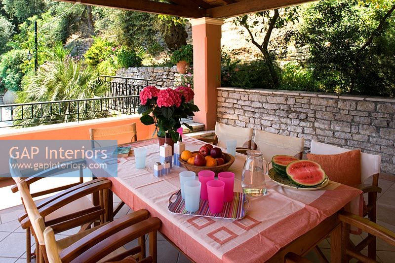 Villa Christina, Kaminaki, Corfu, Greece. Covered outdoor terrace dining area with wooden table and chairs set for alfresco dining