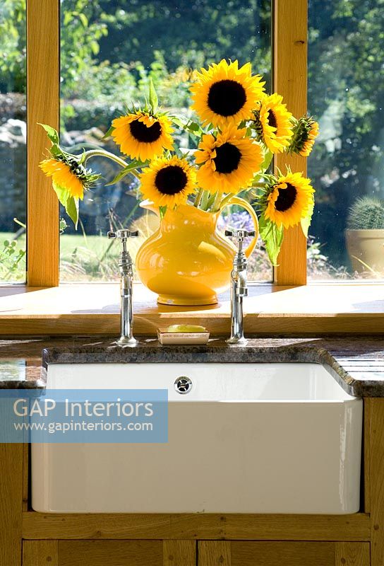 Detail of butler sink in kitchen with vase of sunflowers and view to garden