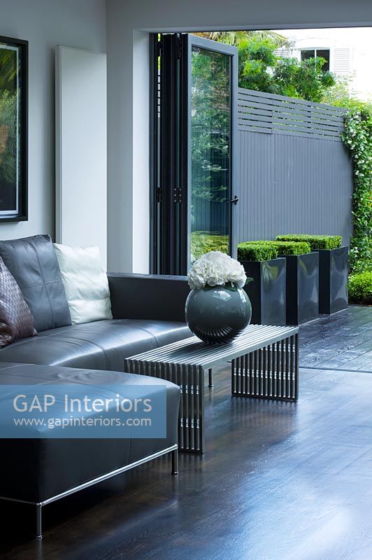 Contemporary living room with grey leather corner sofa, vase and coffee table, leading out to patio and garden designed by Charlotte Rowe