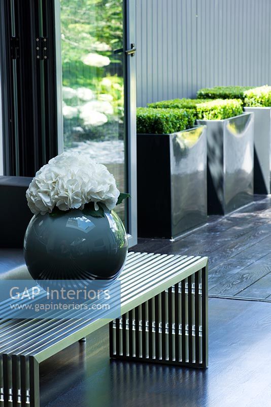 Detail of contemporary vase and low level metal coffee table with view through patio doors to garden