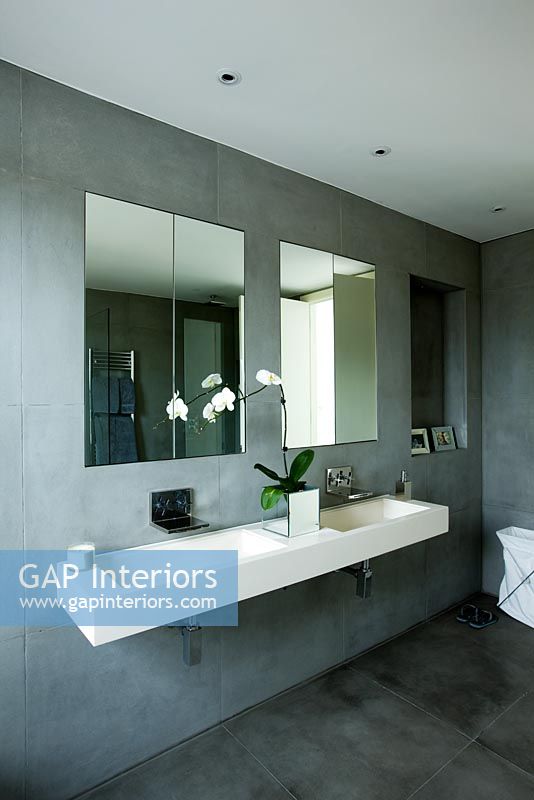 Stylish contemporary bathroom with wall mounted double stone sink, grey slate walls, mirrors and white orchid
