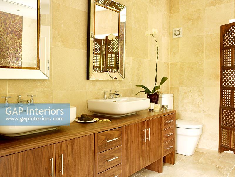 Modern bathroom with twin basins and dark wood cupboards  Large sandstone tiles and wooden screen