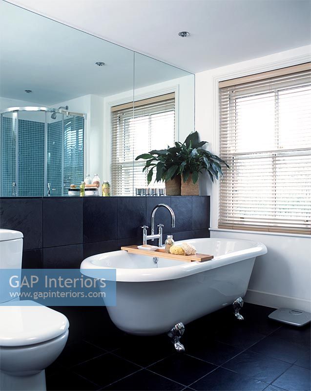 Classic bathroom with freestanding roll top bath, large mirror and black slate wall and floor tiles 