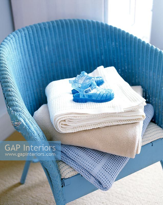 Detail of blue chair with folded blankets and childs shoes 