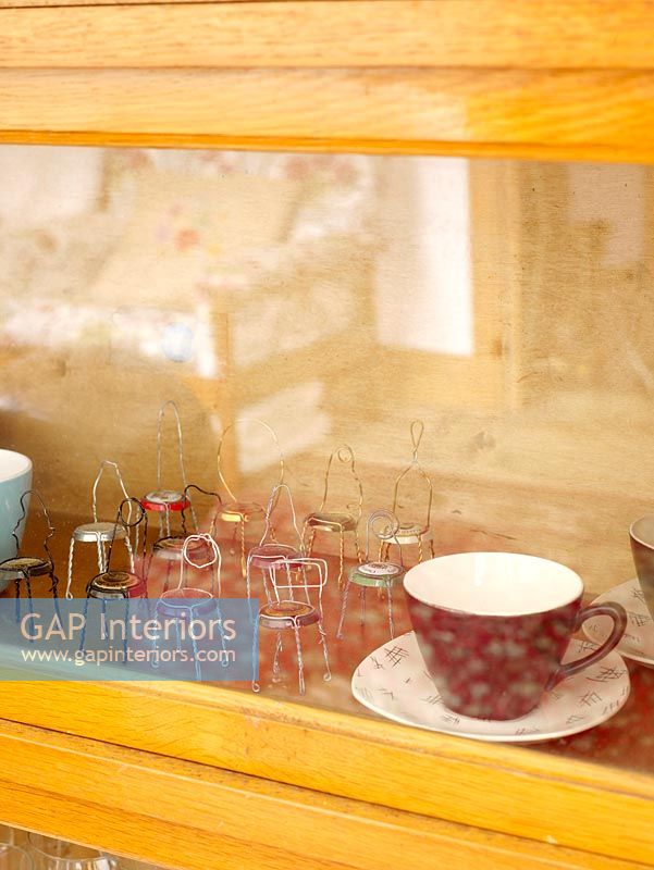 Detail of glass display cabinet with cups and small chairs maid from bottle tops