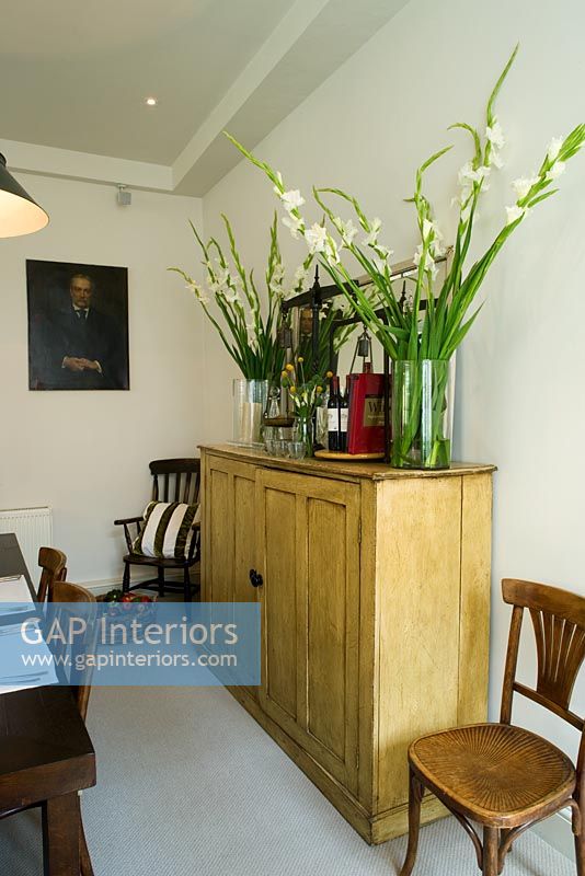 Wooden cabinet with glass jars filled with white gladioli in dining room