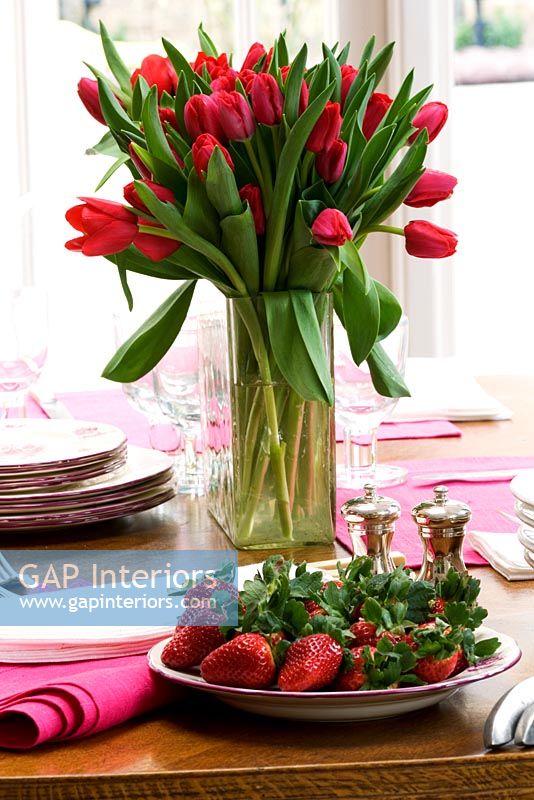 Red tulips in a vase and plate of strawberries on dining table
