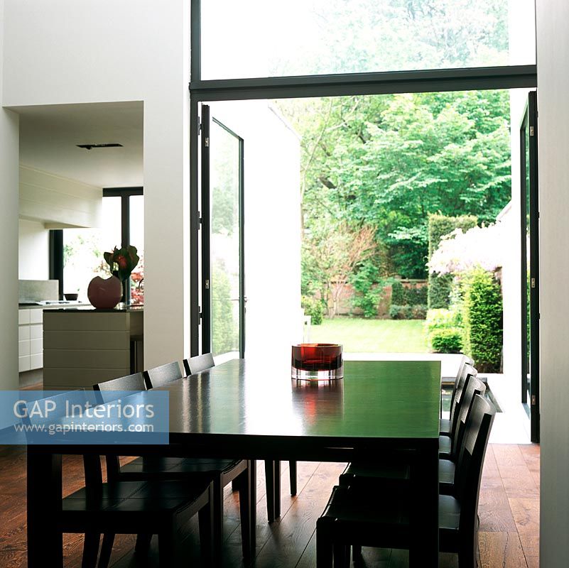 View of dining table with kitchen and open doors to garden in background