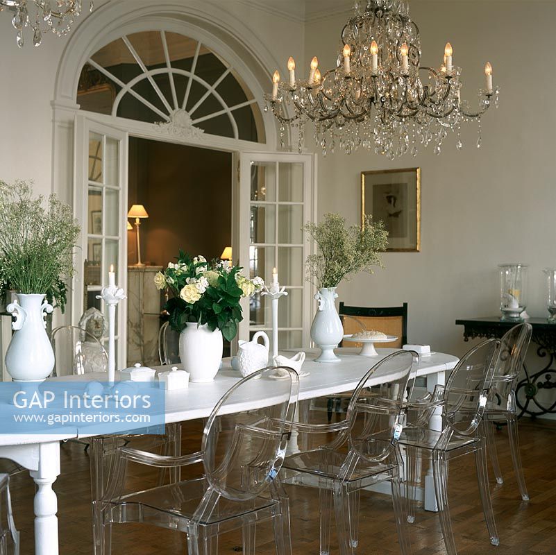 Vase of flowers on dining table with illuminated chandelier and Louis Ghost chairs