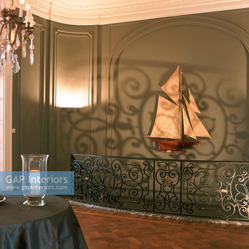 Illuminated candle on table on landing with decorative bannisters and model ship on wall