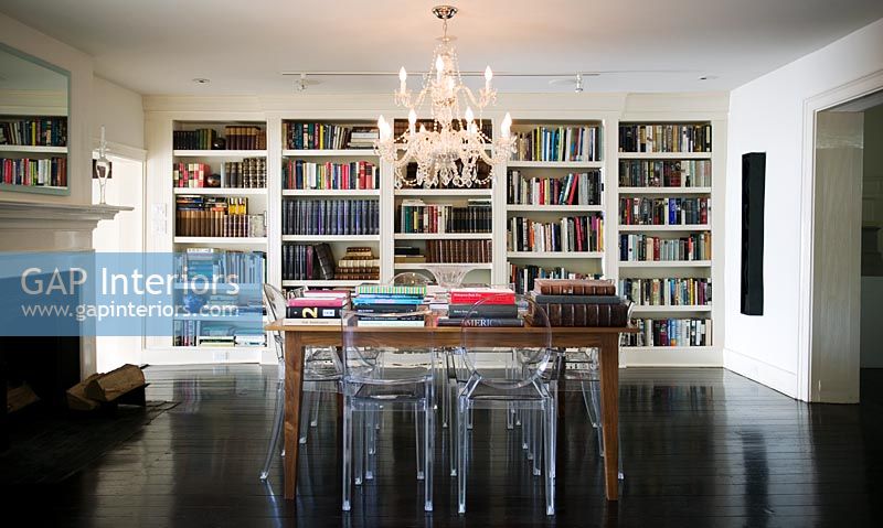 Wooden table surrounded by Louis Ghost chairs in room with large bookcase