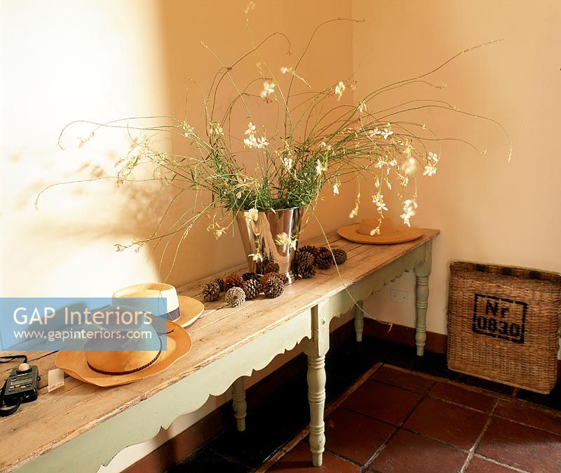 Long wood console with straw hats, a bouquet of flowers and pine cones