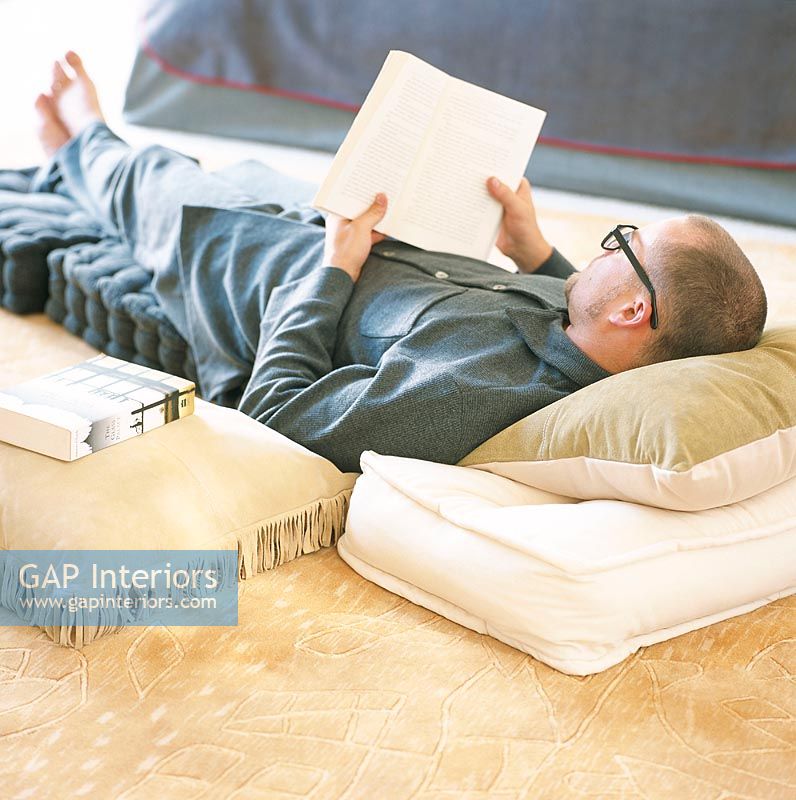 Man lying on cushions reading