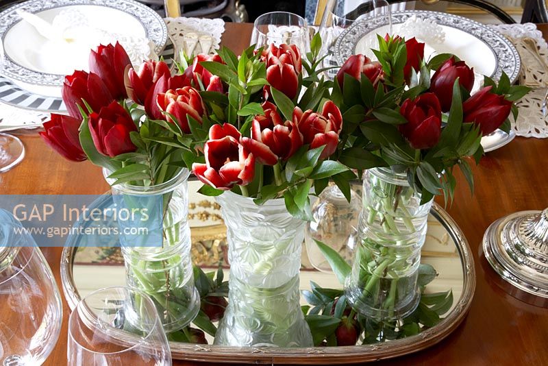 Dinning table detail of three cut glass vases with red tulips
