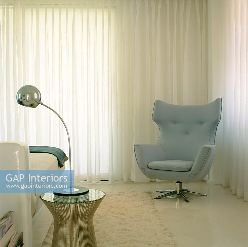 A contemporary grey armchair next to white curtains