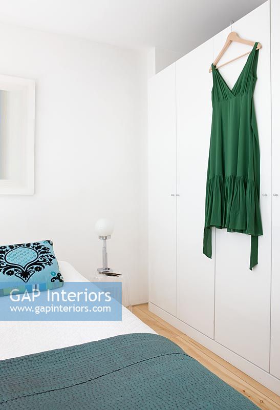 Bedroom with turquoise patterned cushion and green dress hanging from the wardrobe