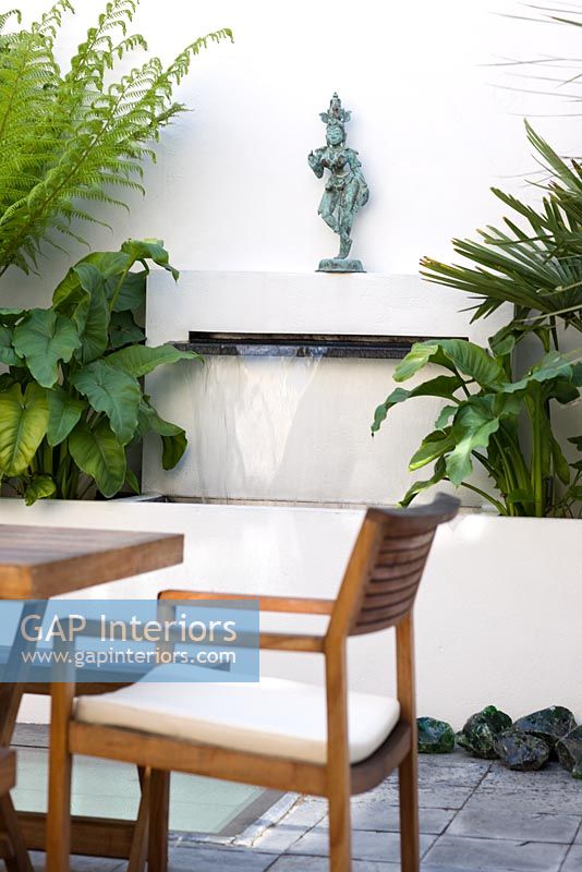 Water feature in small urban garden with statue on built in shelf above