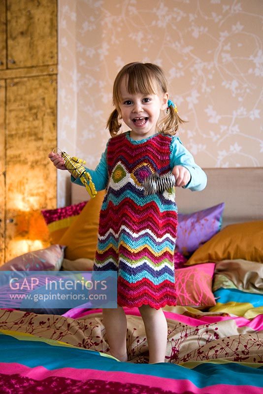 Little girl bouncing on colourful bed