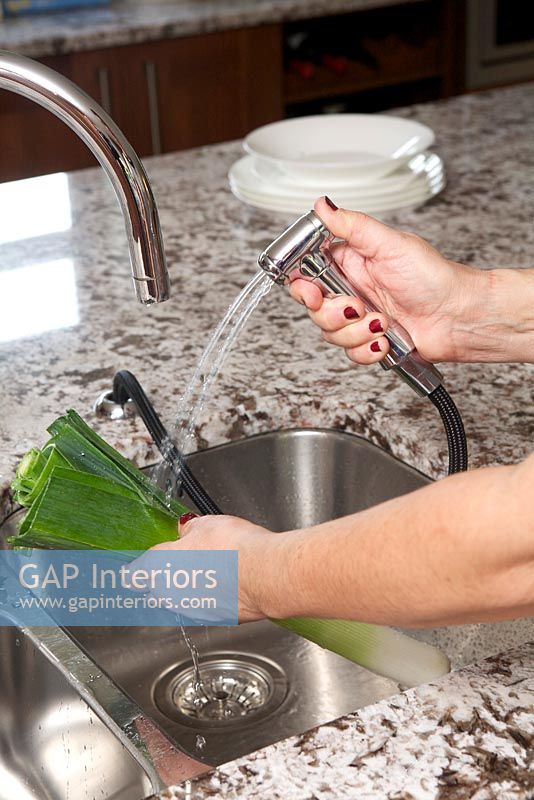 Woman using spray tap to wash vegetables 