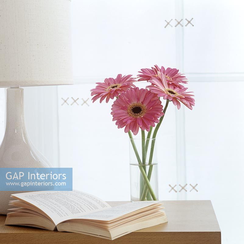 Vase of flowers on table with book and lamp 