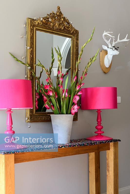 Pink Gladioli and lamps on console table