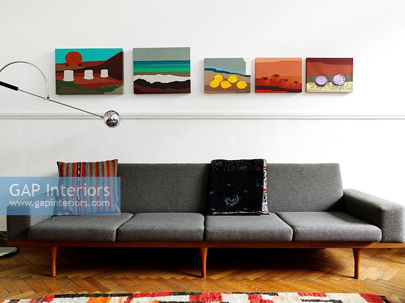 Colourful paintings hung above retro sofa