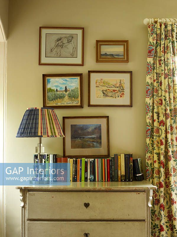Framed paintings above vintage chest of drawers