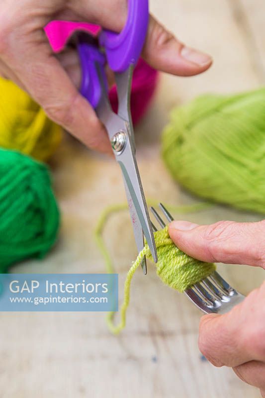 Making christmas pompom decorations - Use the scissors to cut the wool, leaving a wound bundle of wool on the fork 
