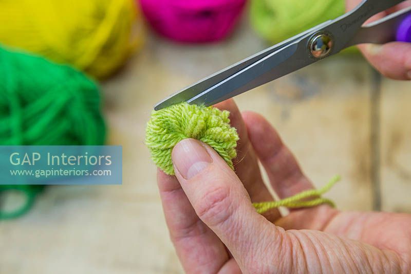 Making christmas pompom decorations - Carefully push the scissor blade into the bundle of wool and cut the strands of wool in half 