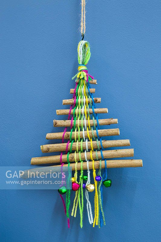 A colourful christmas tree made with sticks coloured wool and miniature baubles against a blue backdrop