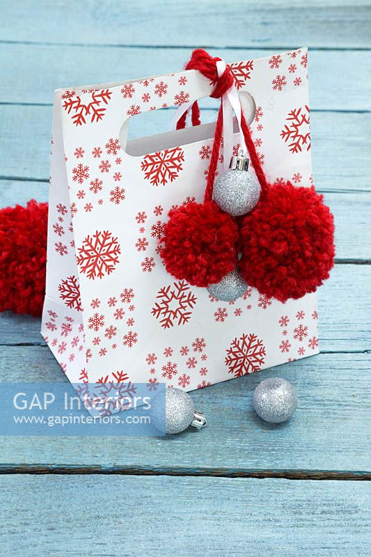 Christmas gift bag decorated with silver baubles and red pompoms made from wool