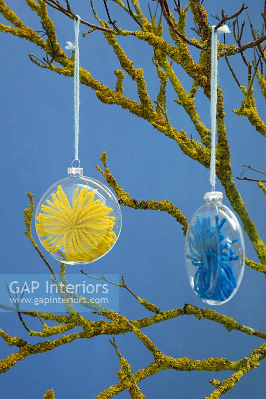 Transparent baubles containing wool stars hanging from a branch covered in Lichen