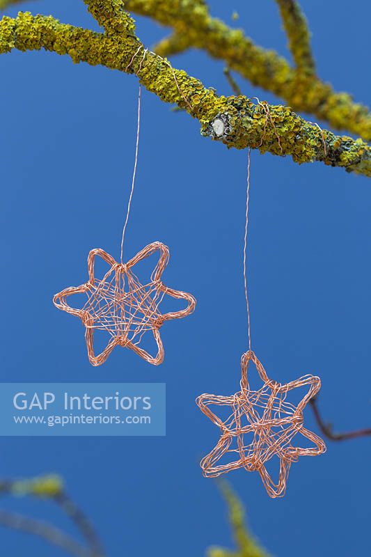 Making copper wire stars - finished decorations hanging from a lichen covered branch against a blue background